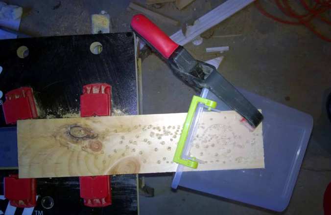 Again, you can probably have someone hold while you drill, but I have the clamps handy, so I use them. Notice the piece of wood underneath, which gives you something to drill in. You can also use the circle created by earlier drillings to line up the hole.
